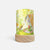 A cylindrical table lamp with a light wood base and a printed fabric shade featuring a whimsical camping scene with a small green gnome, a teepee tent, and a dog, shown on a light gray background.