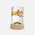 A cylindrical table lamp with a light wood base and a printed white shade featuring a whimsical winter illustration of a figure riding a fox over snow, with a small green door and house at the bottom.