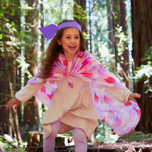 Child in a forest wearing a colorful cape and purple headband