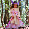 Young girl in a forest wearing a dress with a large pink bow and purple headband.