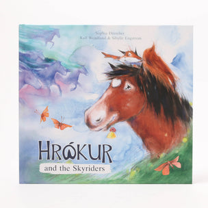 Children's book cover titled 'Hrókur and the Skyriders' featuring a painted brown horse with a dark mane against a dreamy blue and purple sky, with butterflies and green grass at the bottom.