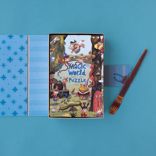 A flat-lay view of a 'Magic World Puzzle' box on a solid blue background, accompanied by a blue star-patterned folder and a wooden wand.
