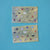Two rectangular gold foil sticker sheets with circular cutouts containing various small illustrated icons, photographed on a solid turquoise-blue background.