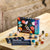 Gemstone collection kit box displayed on a light wood table with several polished and raw gemstones scattered around it. The box reads 'Gemstone Collection' and 'Science Museum,' with a small card in front showing 'Gemstone ID.