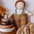 A soft Waldorf fabric doll with curly brown hair, a light blue shirt, and tan overalls sits among wooden toys, including a stack of round pegs and a wooden horse.