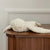 White plush toy resembling a dolphin on a wooden surface with a neutral wall background