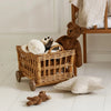 Wooden crib with a wicker toy cart containing stuffed animals on a white floor.