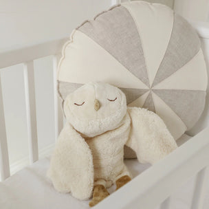 Plush owl toy in a crib with geometric-patterned pillow