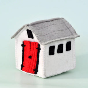 A small handmade felt house toy or decoration with a white body, gray roof, and bright red door, shown on a pale blue background.