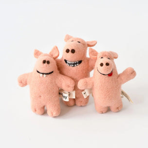 Three small pink felt pig toys with embroidered faces and small tags, standing together on a clean white background.
