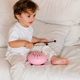 Child playing with a pink drum on a white couch
