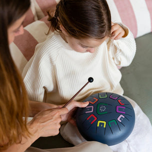 Two people sitting on a couch with a colorful handpan, one person holding a drum stick