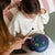 Two people sitting on a couch with a colorful handpan, one person holding a drum stick