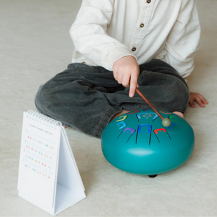 Child playing with a drum on a light-colored floor.
