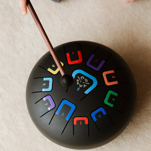 Black drum with colorful symbols on a beige surface, held by a child's hand.