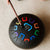 Black drum with colorful symbols on a beige surface, held by a child's hand.