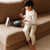 Child playing with a small drum on a beige couch in a bright room.
