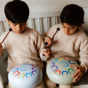 Two children playing with colorful drums indoors.