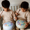 Two children playing with colorful drums indoors.