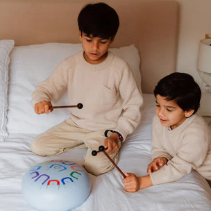 Two children playing with musical instruments on a bed.