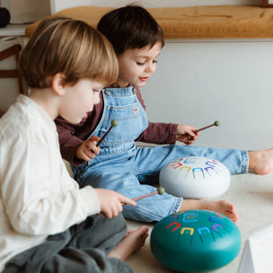 Two children playing with musical instruments on a light-colored floor.