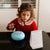 Child playing with a blue drum on a table next to a calendar