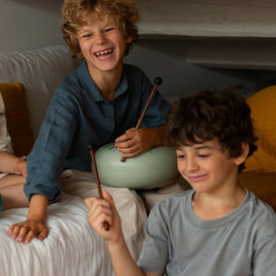 Two children playing with colorful drums on a couch.
