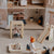 A miniature wooden dollhouse interior with tiny furniture pieces, a small slide, a swing, and tiny figurines playing on a beige carpeted floor.