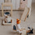 A set of wooden children's playground toys arranged on a beige textured floor, including a swing set, a slide, a seesaw, and small character figures.