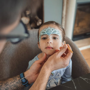 Person applying face paint to a child's face in a casual indoor setting