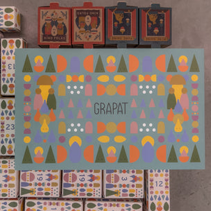 A flat-lay view of a Grapa advent calendar, showing the central decorated box with the brand name 'GRAPAT' and surrounding numbered boxes on a concrete floor.