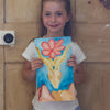 Young girl holding a painting of a flower and deer against a wooden door.