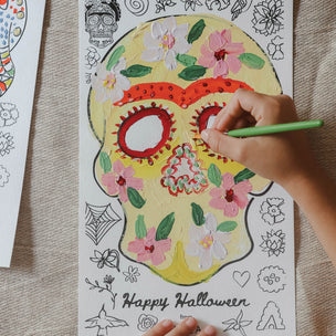 Coloring page of a floral skull with 'Happy Halloween' text, being colored by a hand.