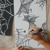 Person coloring a spider web design on a piece of paper with a marker.