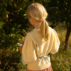 Young girl in a yellow sweater and pink skirt standing in a natural setting.
