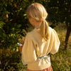 Young girl in a yellow sweater and pink skirt standing in a natural setting.