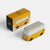 Yellow and white model of a Volkswagen bus next to its packaging box on a light gray background
