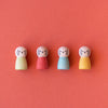 Four colorful wooden peg dolls with face paint on a pink background