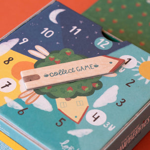 Colorful card game box with a wooden piece labeled 'collect GAME' on an orange surface