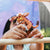 Person holding a small plush toy with a colorful face against a blurred outdoor background