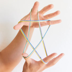 Hands playing with colorful string on a plain background