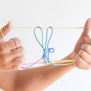 Hands holding a bow made of colorful yarn against a white background