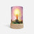 A cylindrical table lamp with a printed watercolor-style design of a glowing candle among crystals, set on a light natural wood base against a plain white background.