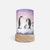 A cylindrical lamp or candle-style decor piece with a watercolor illustration of penguins on a snowy landscape, mounted on a round light wood base against a clean white background.
