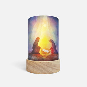 A cylindrical LED candle lamp with a light wood base, featuring a printed graphic of the Holy Family under a glowing star.