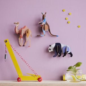 Studio Roof Colorful animal-shaped wall hooks on a pink wall with a yellow toy crane in the foreground.