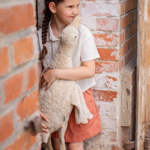 Young girl holding a stuffed animal against a brick wall