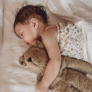 Child sleeping with a teddy bear on a soft surface