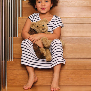 Child sitting on wooden steps holding teddy bears, wearing a striped dress.