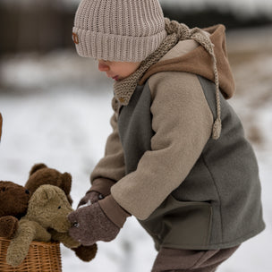 Child in winter clothing interacting with teddy bears in a snowy setting